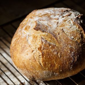 Fresh homemade bread made of sourdough resting on a wire rack. Artisan bread with golden crispy crust.