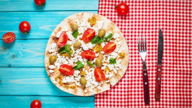 Pita with cheese, cherry tomatoes, olives and greenery on blue wooden background.